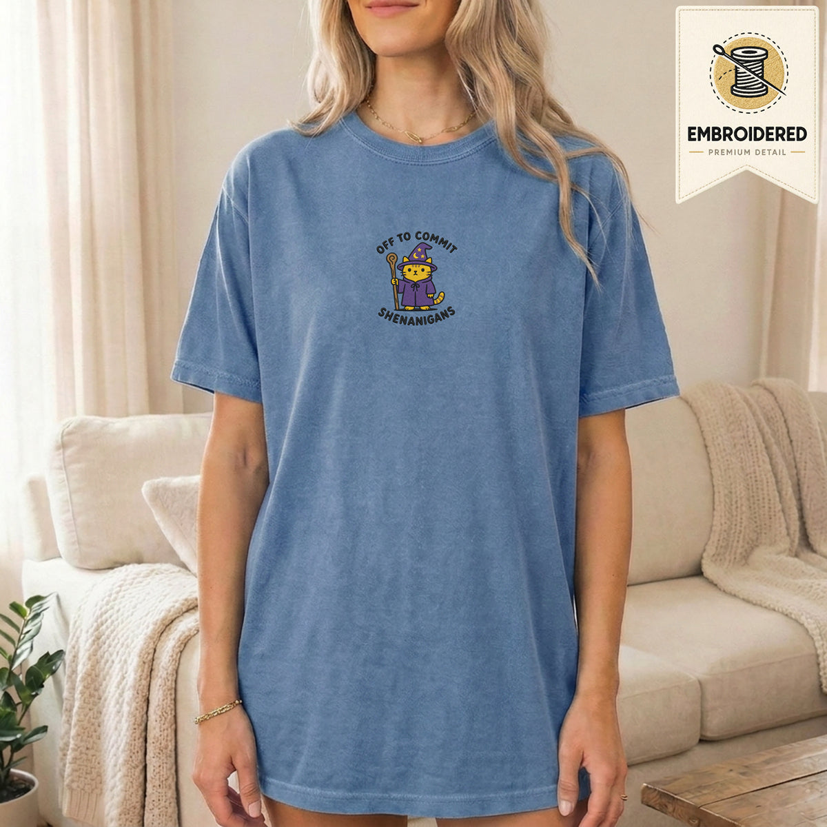 Woman wearing a blue jean embroidered funny cat t shirt with Commit Shenanigans cat design while standing indoors