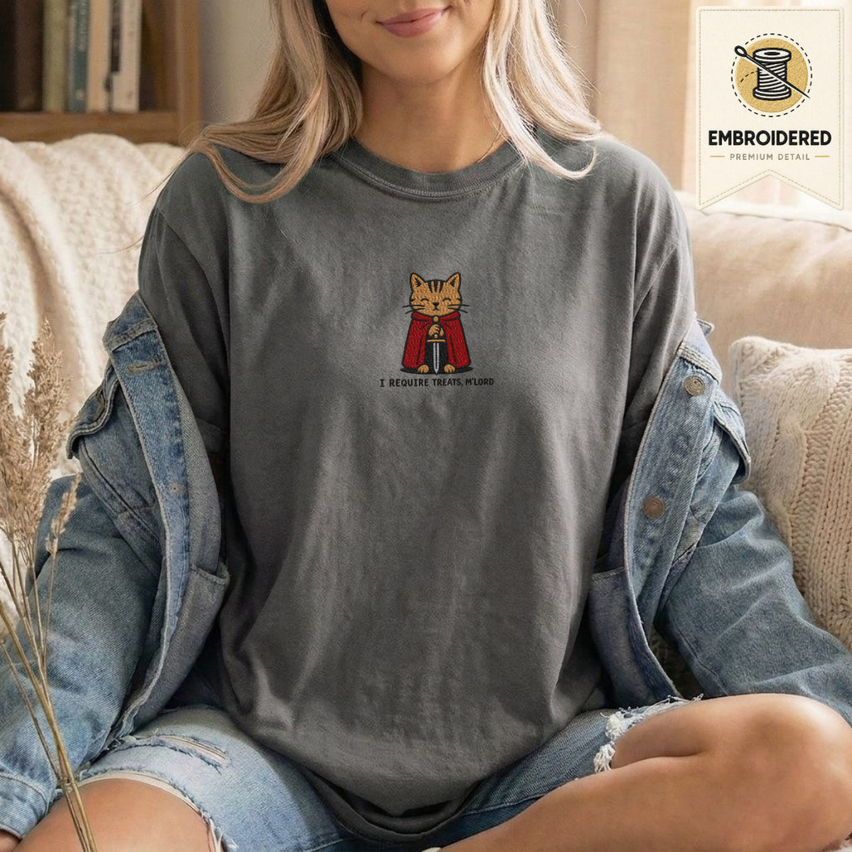 Woman wearing a pepper gray embroidered funny cat t shirt with Require Treats cat design while sitting indoors in a denim jacket