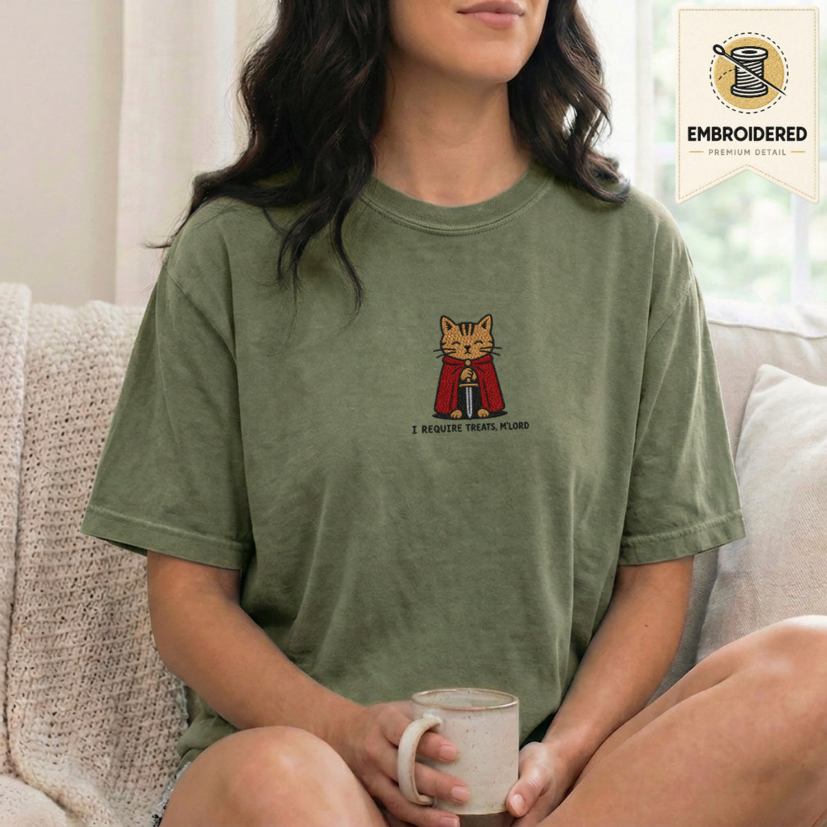 Woman wearing a moss green embroidered funny cat t shirt with Require Treats cat design while sitting indoors