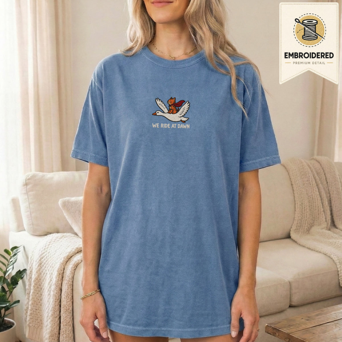 Woman wearing a blue jean embroidered funny cat t shirt with We Ride At Dawn cat design while standing indoors