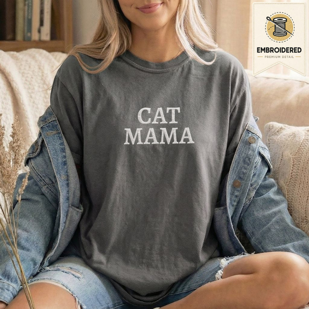 Woman wearing a pepper gray embroidered cat mama t shirt with Cat Mama text while sitting indoors in a denim jacket
