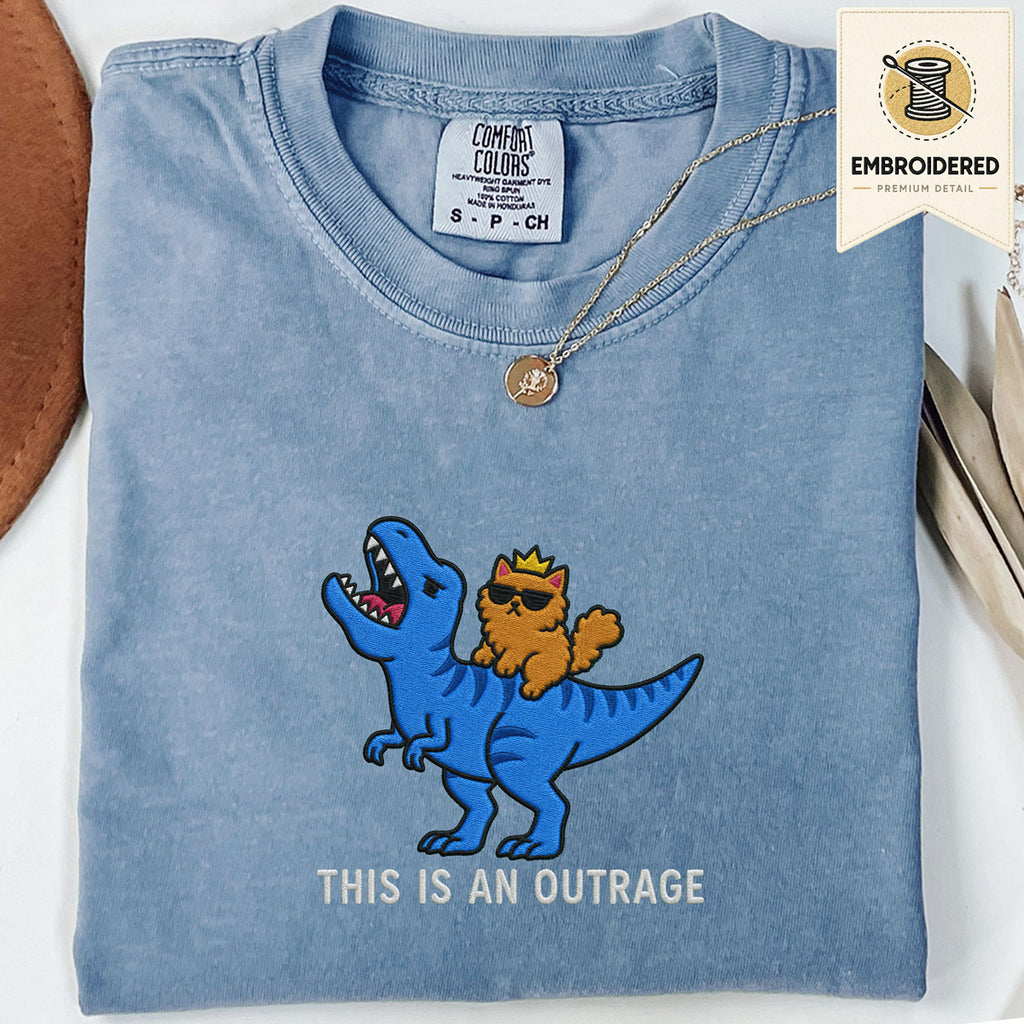 Woman wearing a moss green embroidered funny cat t shirt with This Is An Outrage cat design while sitting indoors