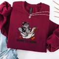 Maroon embroidered cat sweatshirt with cool grey cat in sunglasses riding a panicking white goose, Born to Honk text, flat lay