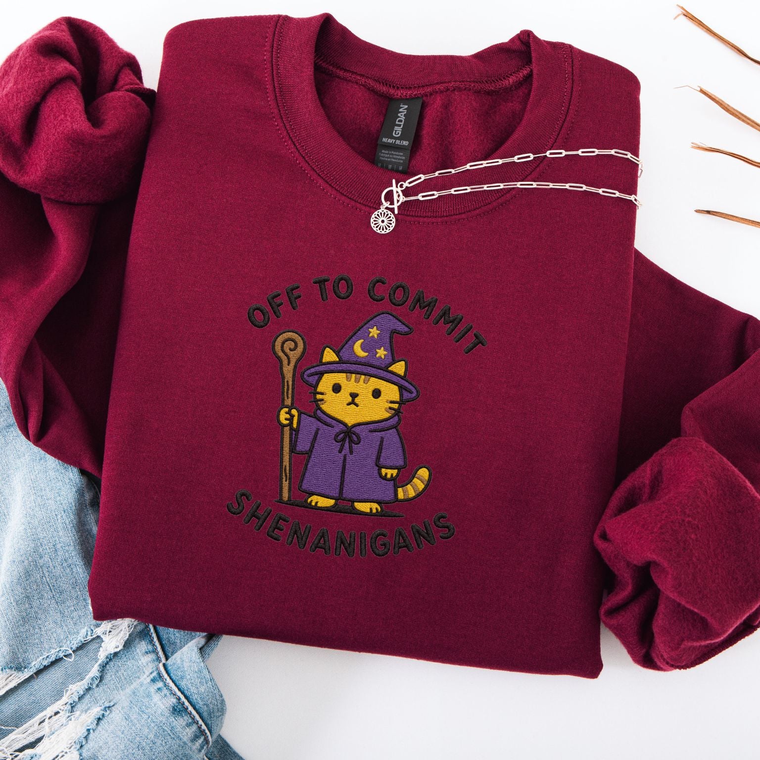 Maroon embroidered cat sweatshirt with orange tabby in purple wizard robe and hat, Off to Commit Shenanigans text, flat lay