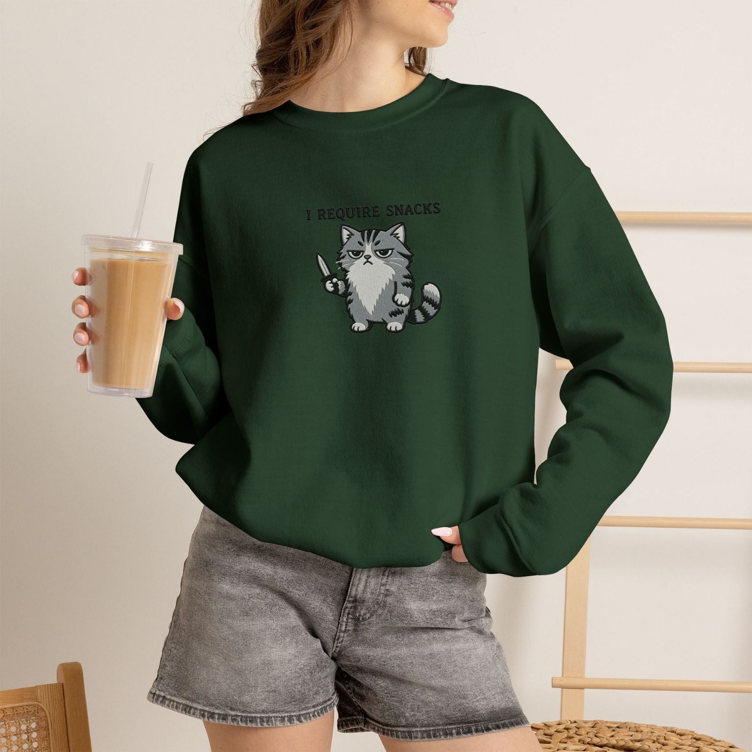 Model wearing navy I Require Snacks embroidered cat sweatshirt, holding iced coffee