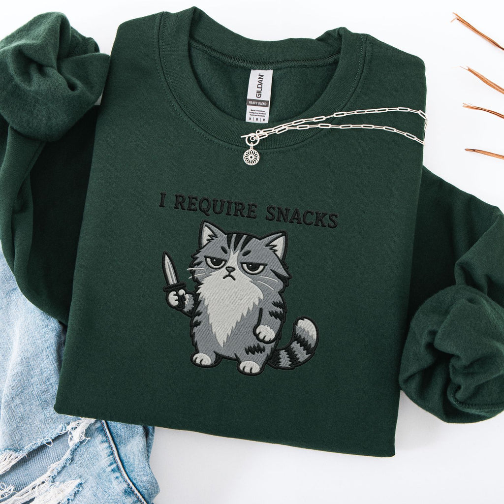 Navy embroidered cat sweatshirt with grumpy grey cat holding a knife, I Require Snacks text, flat lay