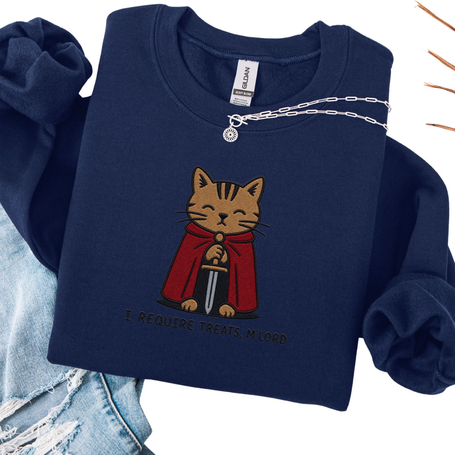 Navy embroidered cat sweatshirt with medieval orange tabby holding a sword, I Require Treats M'Lord text, flat lay