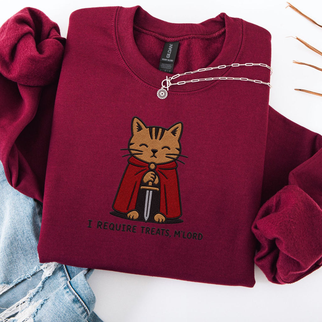 Maroon embroidered cat sweatshirt with medieval orange tabby holding a sword, I Require Treats M'Lord text, flat lay
