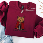 Maroon embroidered cat sweatshirt with medieval orange tabby holding a sword, I Require Treats M'Lord text, flat lay
