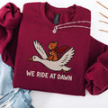 Maroon embroidered cat sweatshirt — caped orange tabby riding a goose, We Ride At Dawn text, flat lay