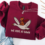 Maroon embroidered cat sweatshirt — caped orange tabby riding a goose, We Ride At Dawn text, flat lay