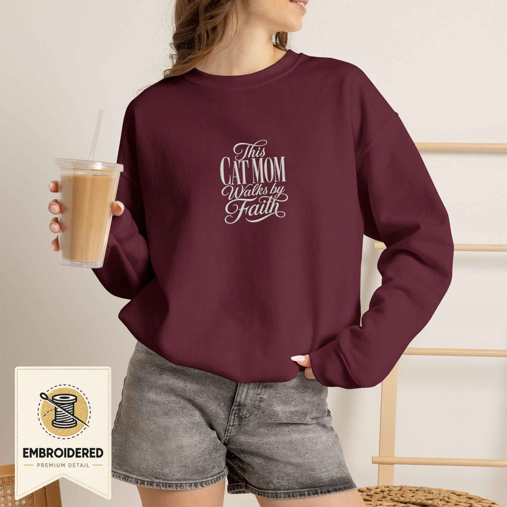 Woman wearing a maroon embroidered This Cat Mom Walks by Faith cat sweatshirt