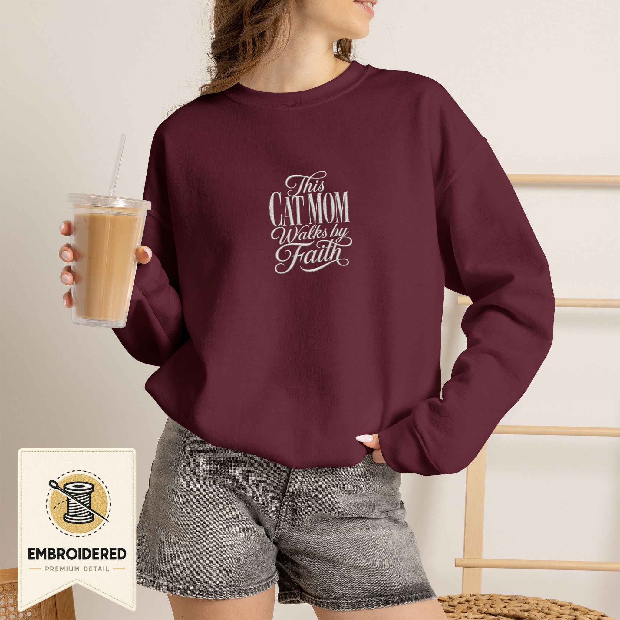 Woman wearing a maroon embroidered This Cat Mom Walks by Faith cat sweatshirt