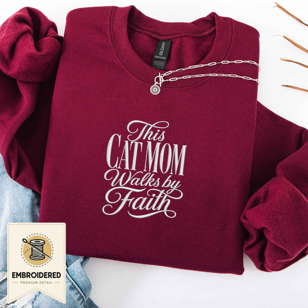 Maroon embroidered cat sweatshirt with a This Cat Mom Walks by Faith script design, shown flat
