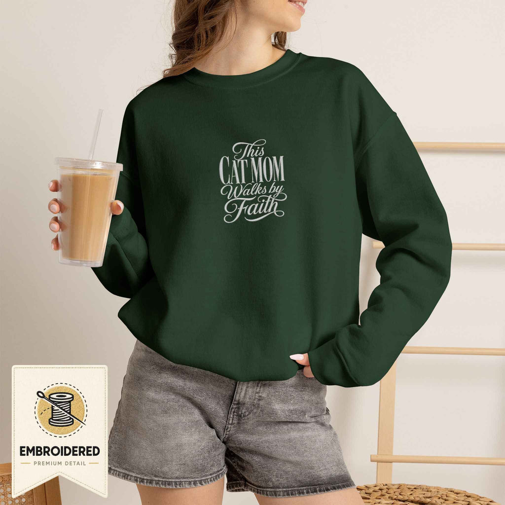 Woman wearing a forest green embroidered This Cat Mom Walks by Faith cat sweatshirt