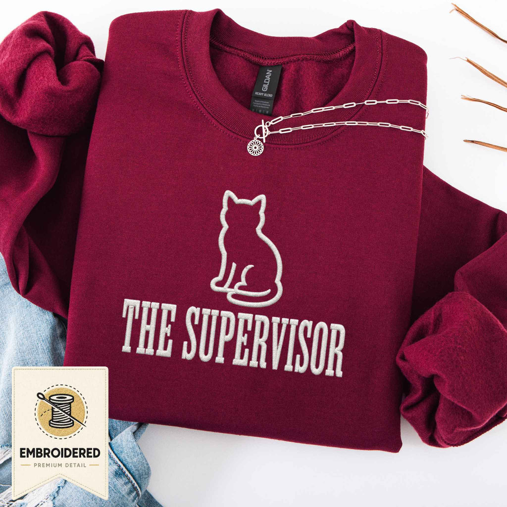 Maroon embroidered cat sweatshirt with a small cat and The Supervisor chest design, shown flat