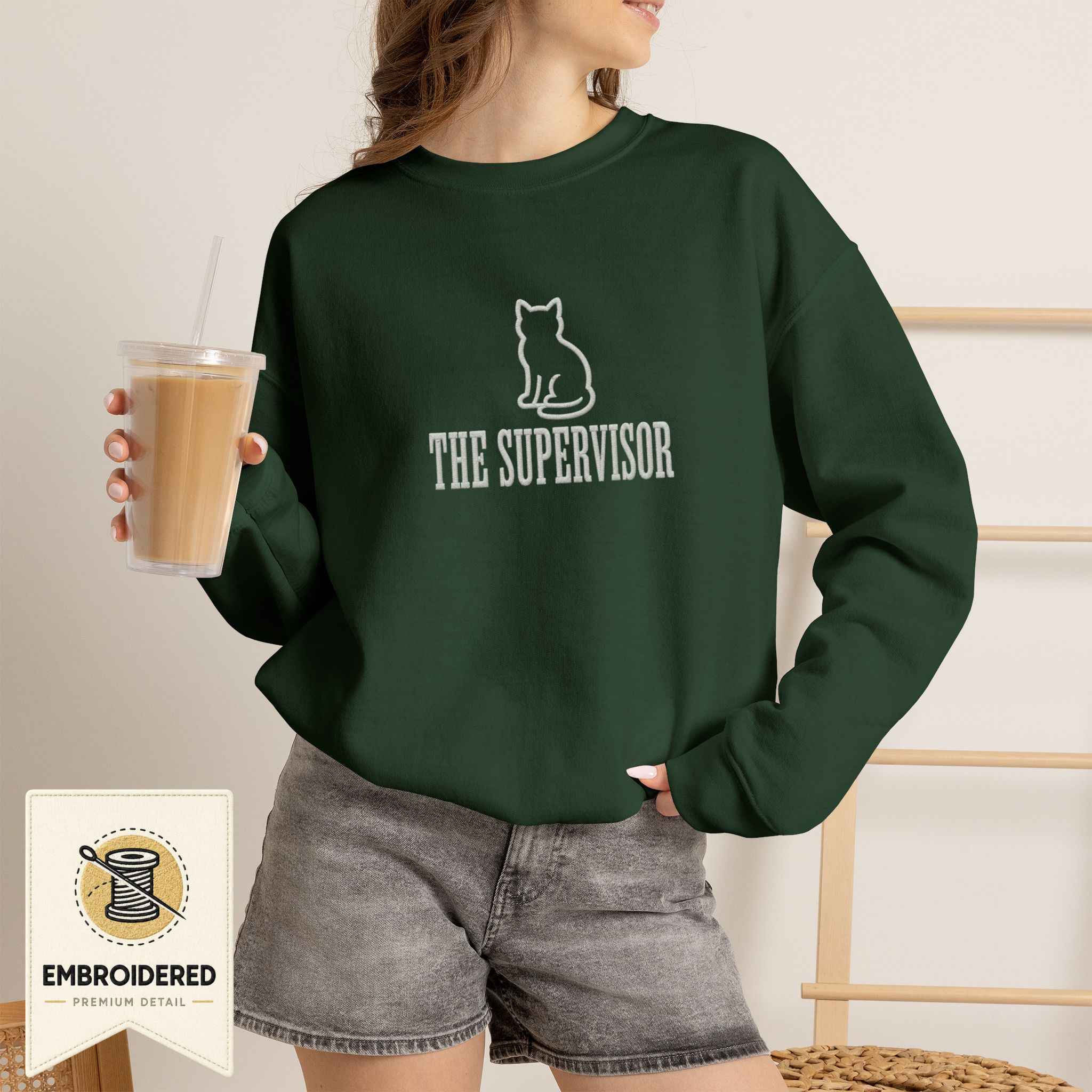 Woman wearing a forest green embroidered The Supervisor cat sweatshirt