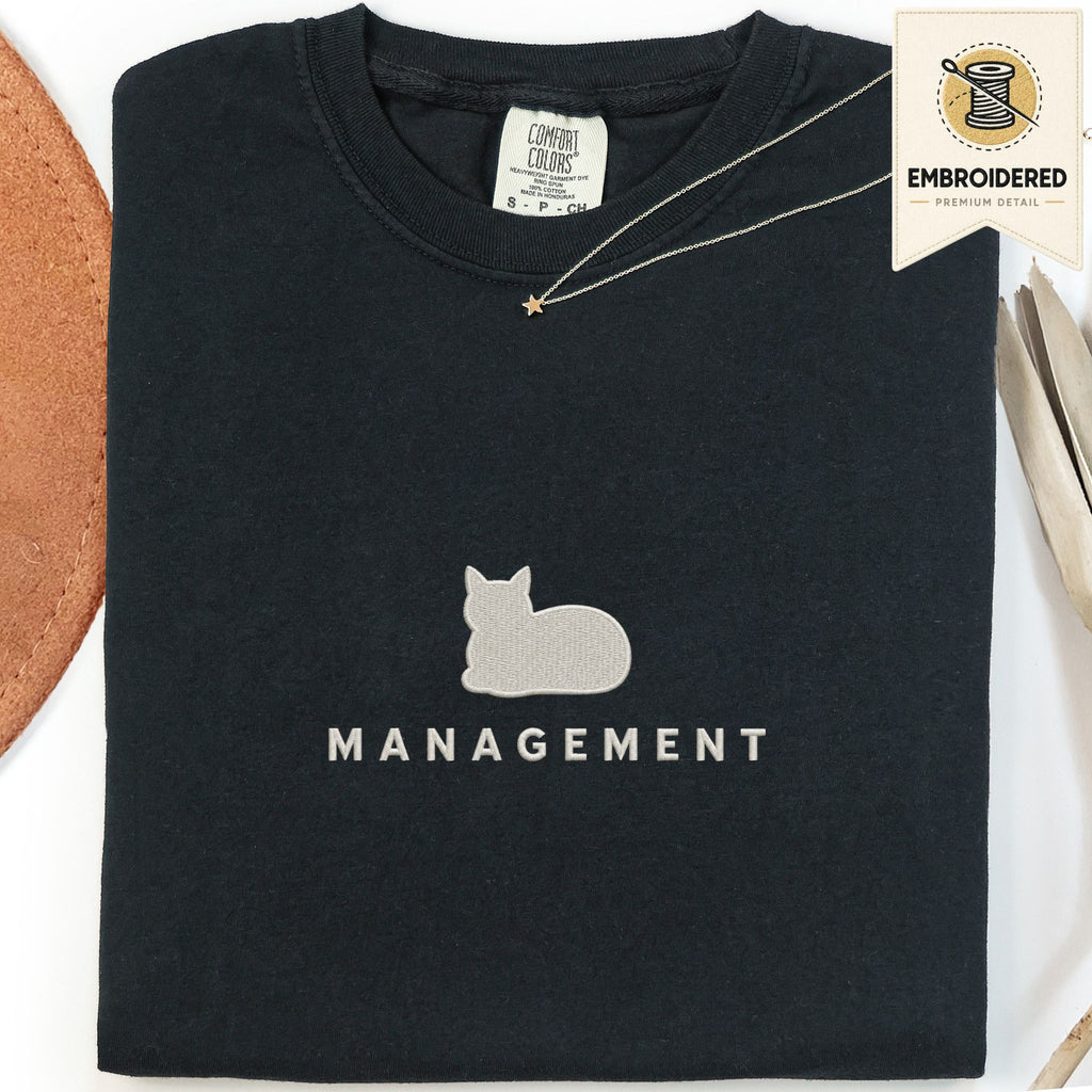 Black embroidered cat t-shirt with a small cat and Management chest design, shown flat