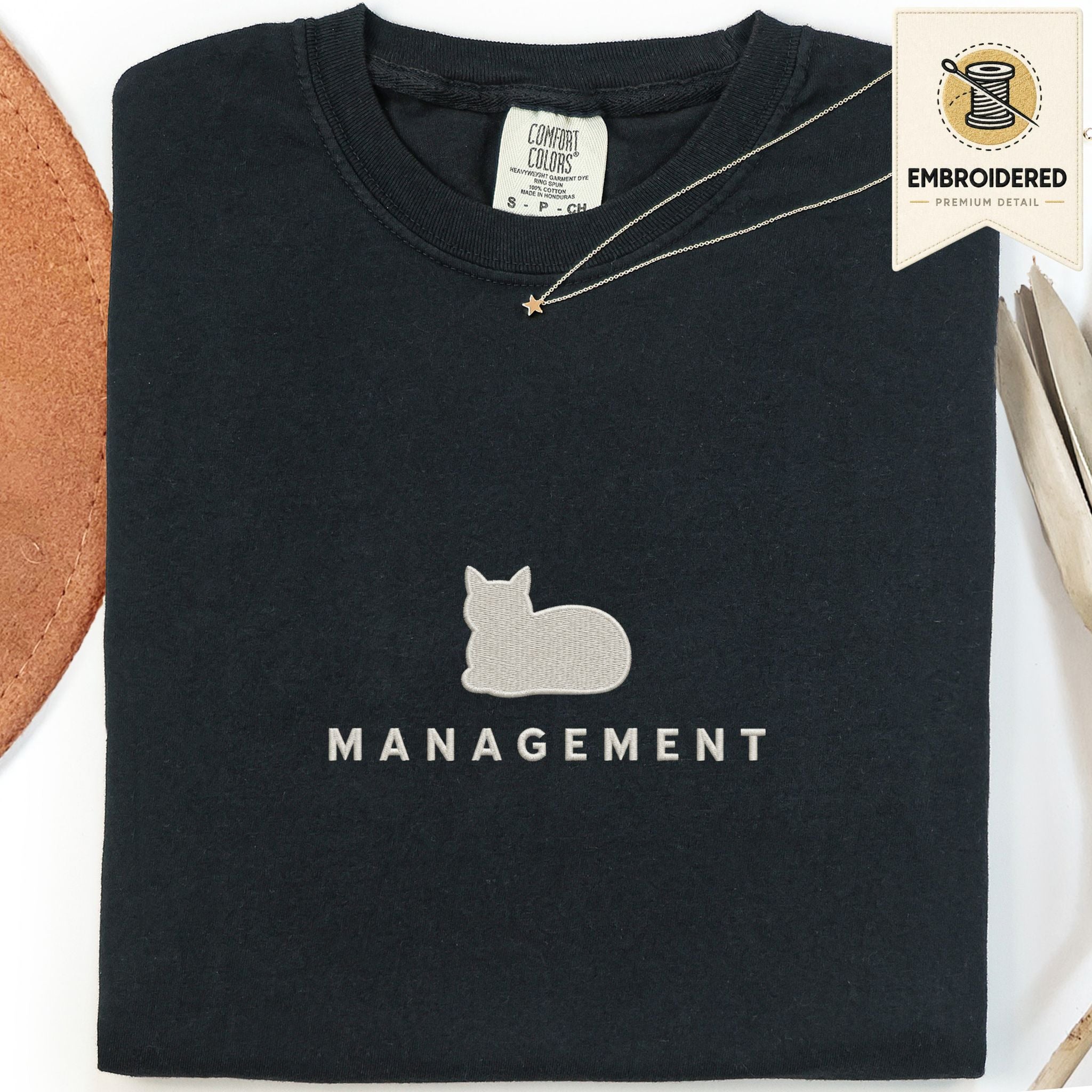 Black embroidered cat t-shirt with a small cat and Management chest design, shown flat
