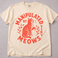 Ivory cat t-shirt with Manipulated By Tiny Meows printed graphic, funny cat lover tee on soft Comfort Colors cotton, flat lay front view