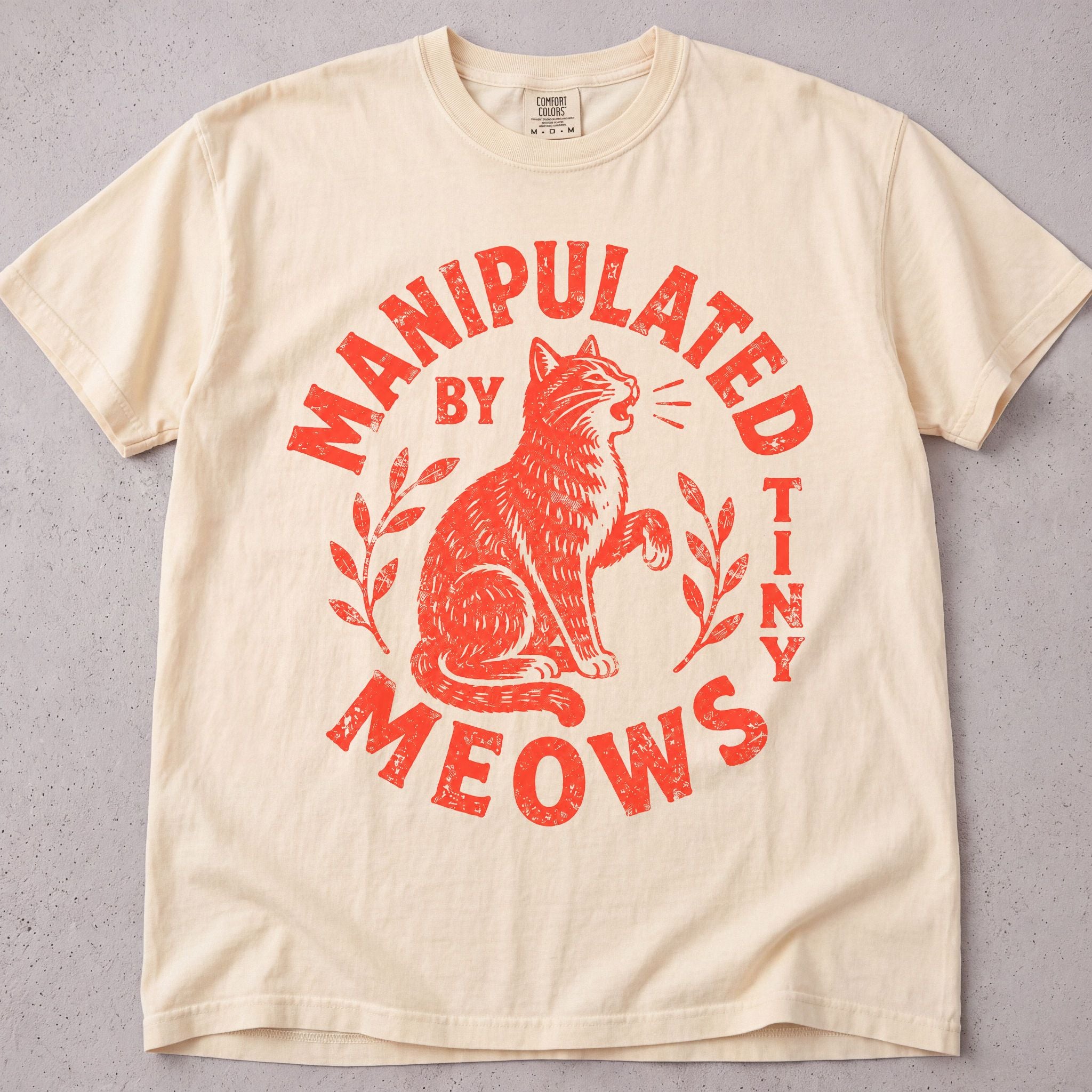 Ivory cat t-shirt with Manipulated By Tiny Meows printed graphic, funny cat lover tee on soft Comfort Colors cotton, flat lay front view