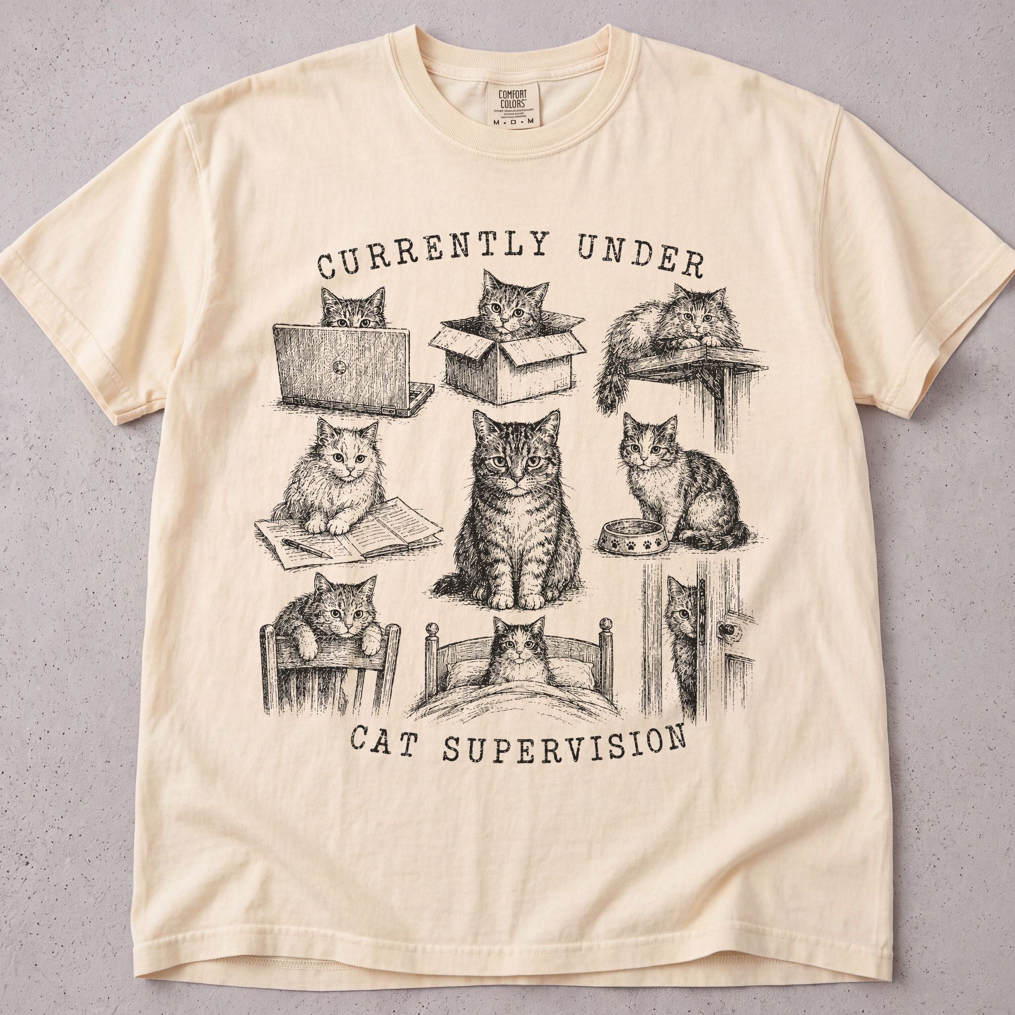 Ivory cat t-shirt with Currently Under Cat Supervision printed graphic, funny cat lover tee on soft Comfort Colors cotton, flat lay front view