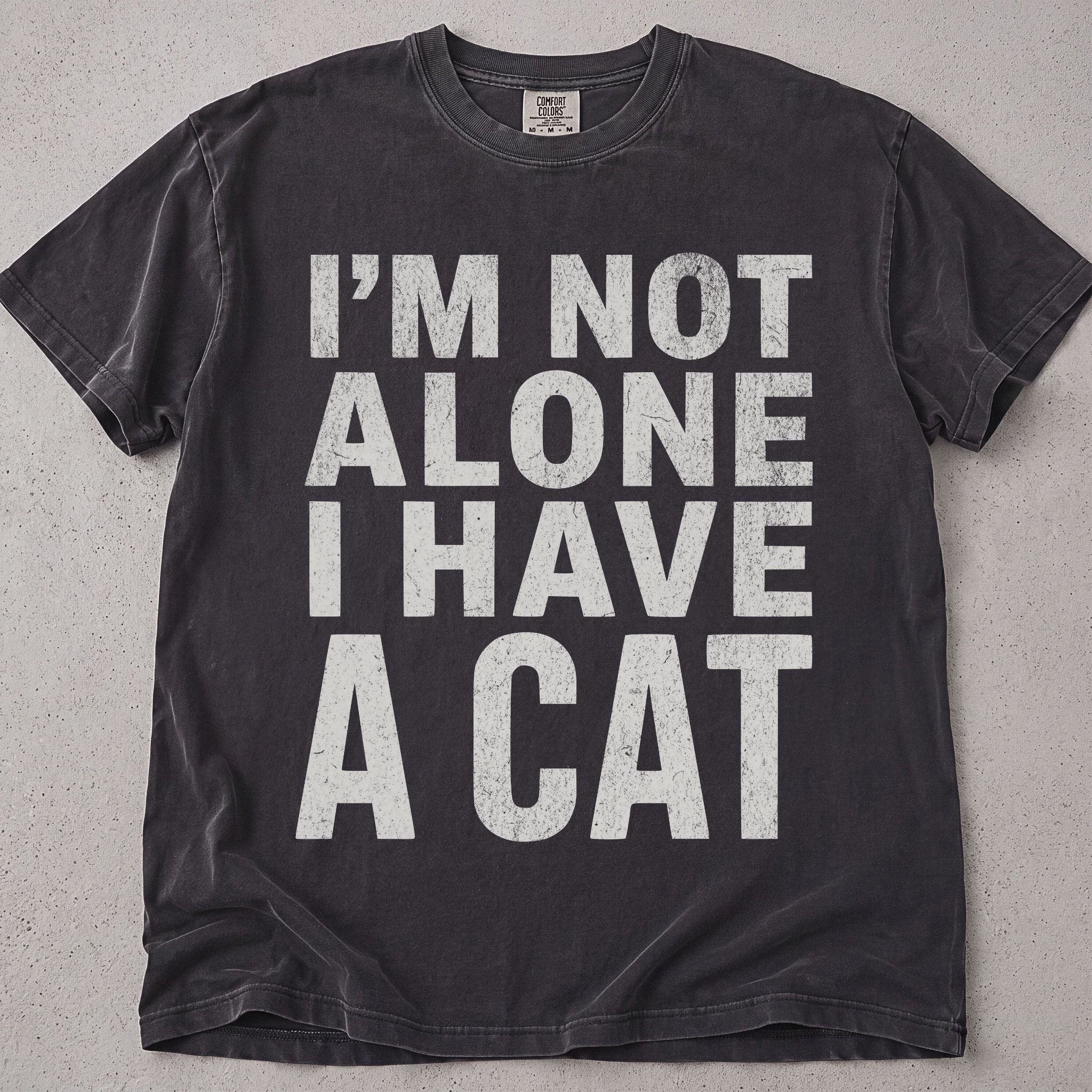 Pepper brown cat t-shirt with I'm Not Alone I Have A Cat printed text graphic, funny cat lover tee on soft Comfort Colors cotton, flat lay front view