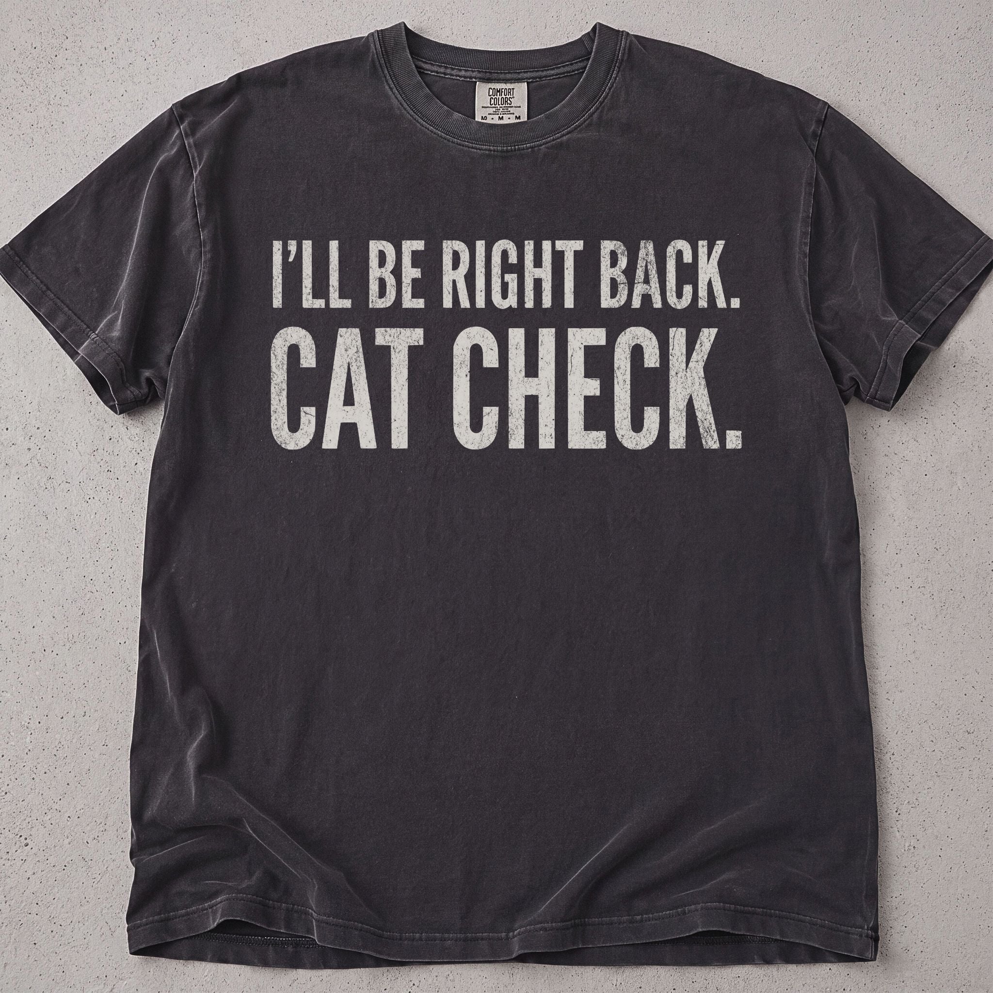 Pepper brown cat t-shirt with I'll Be Right Back Cat Check printed text graphic, funny cat lover tee on soft Comfort Colors cotton, flat lay front view