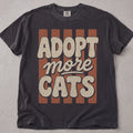 Pepper brown cat t-shirt with a retro groovy Adopt More Cats striped text graphic, cat lover tee on soft Comfort Colors cotton, flat lay front view