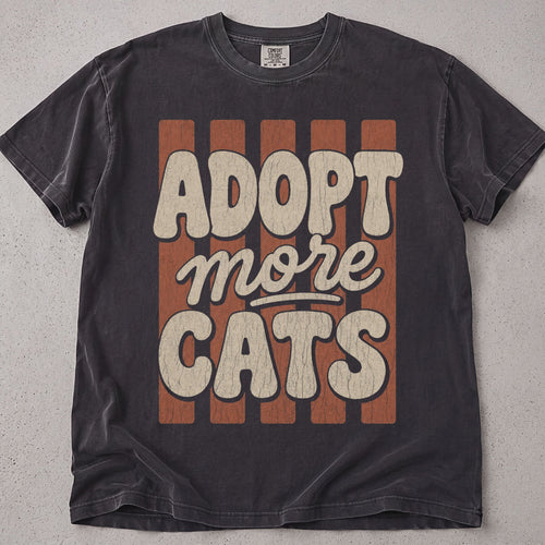 Pepper brown cat t-shirt with a retro groovy Adopt More Cats striped text graphic, cat lover tee on soft Comfort Colors cotton, flat lay front view