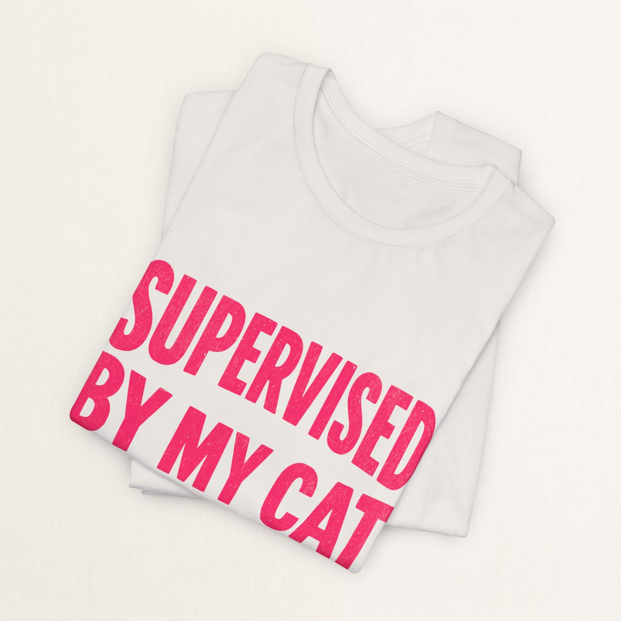 Folded vintage white Supervised By My Cat t-shirt with pink comic-style graphic