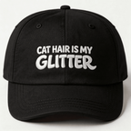 Front view of a black embroidered classic dad cap with white text that says "CAT HAIR IS MY GLITTER"