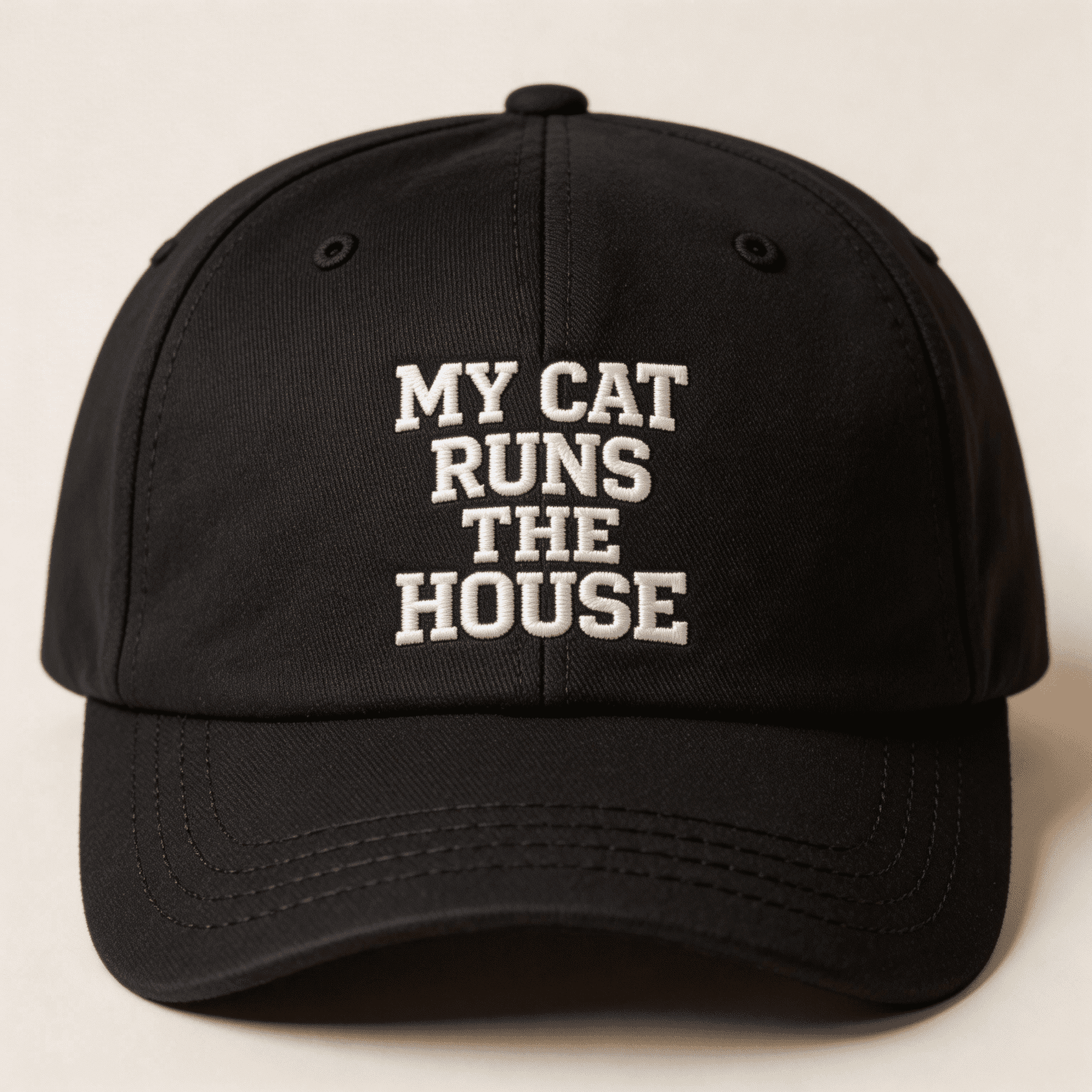 Front view of a black embroidered baseball cap with white text that says "MY CAT RUNS THE HOUSE"