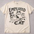 Ivory cat t-shirt with an Employed By My Cat illustration of a cat with a coffee mug, funny cat lover tee on soft Comfort Colors cotton, flat lay front view