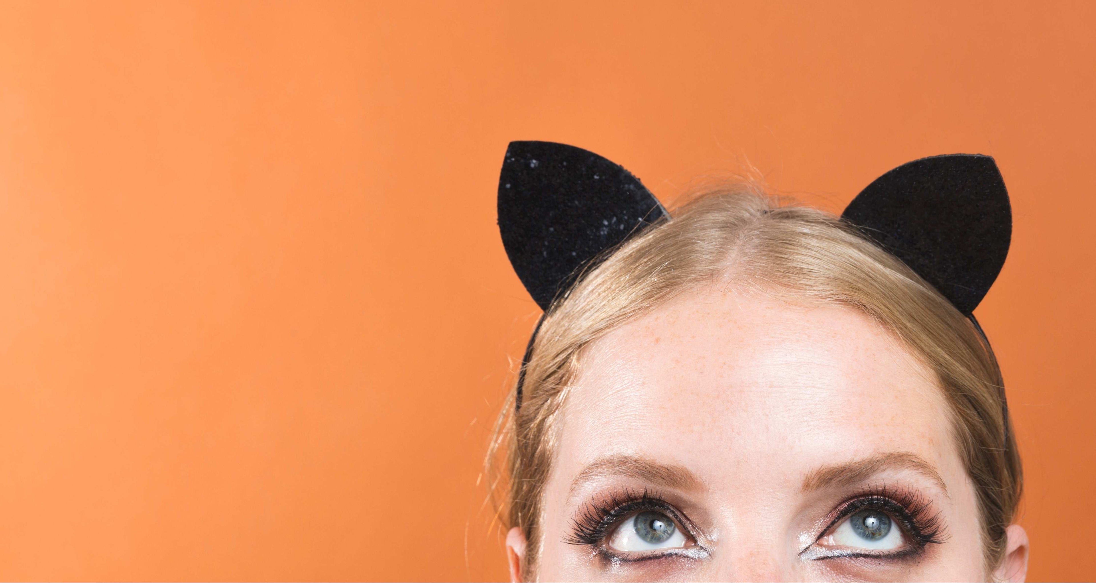Person wearing black cat ears on an orange background