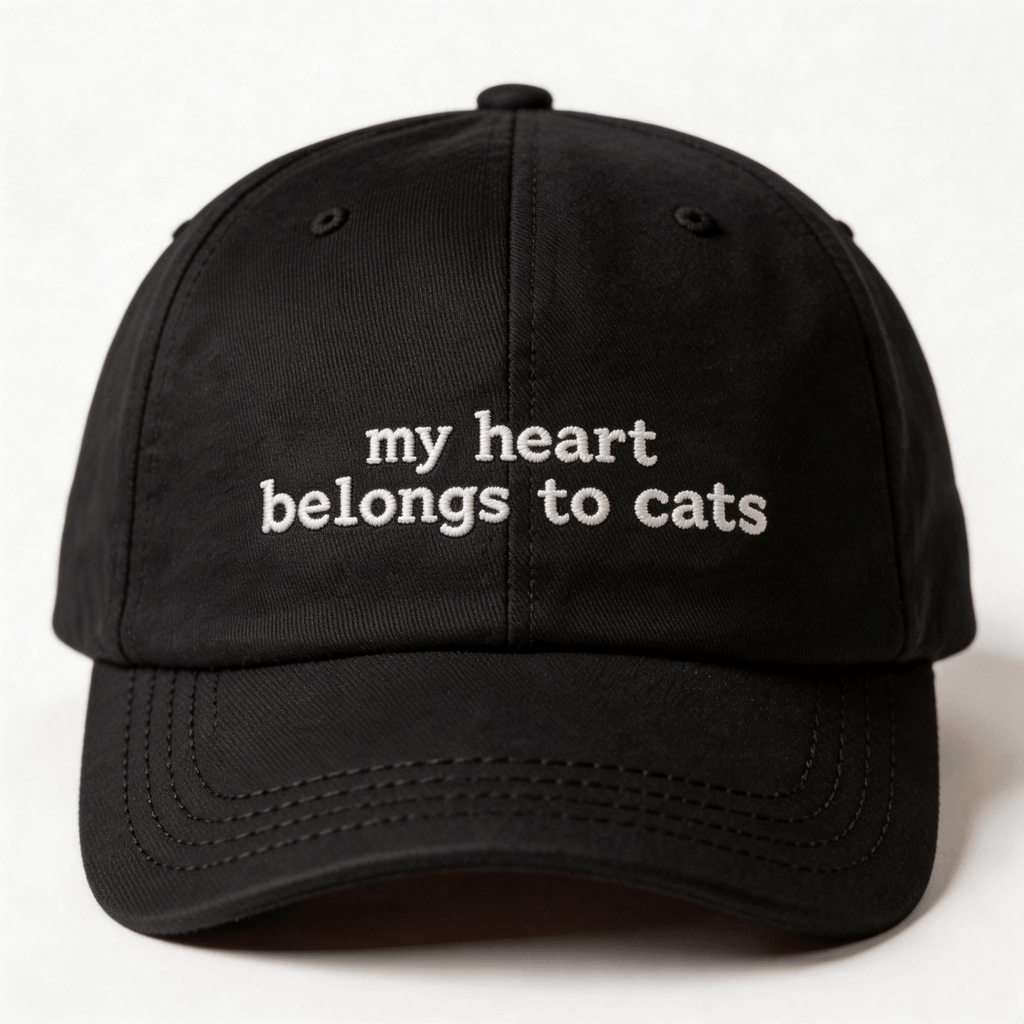 Front view of a black embroidered cap with the phrase my heart belongs to cats in white lettering