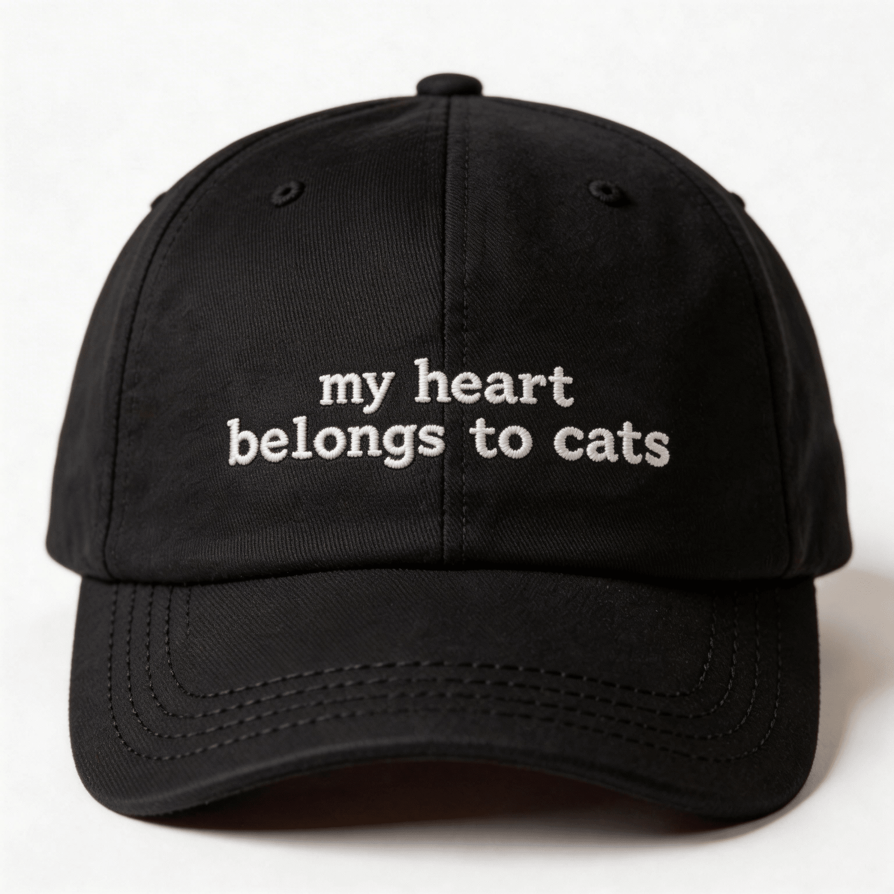Front view of a black embroidered cap with the phrase my heart belongs to cats in white lettering